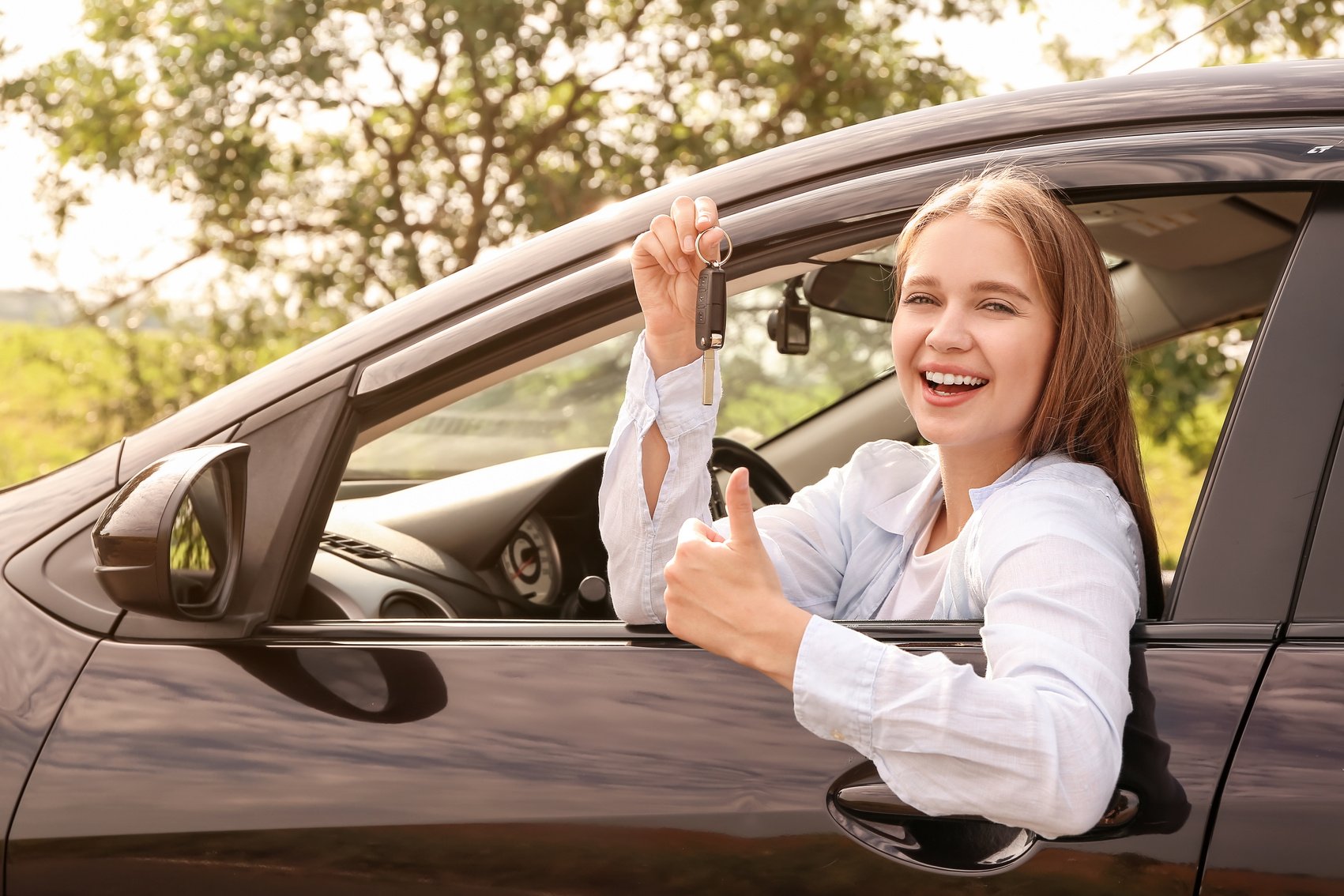 Happy Young Woman with Key Sitting in New Car